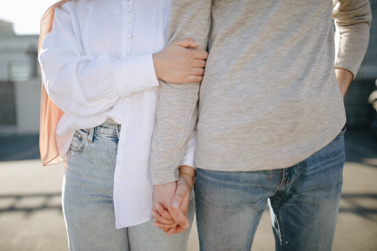 A close-up view of a couple holding hands and wearing casual attire outdoors.
